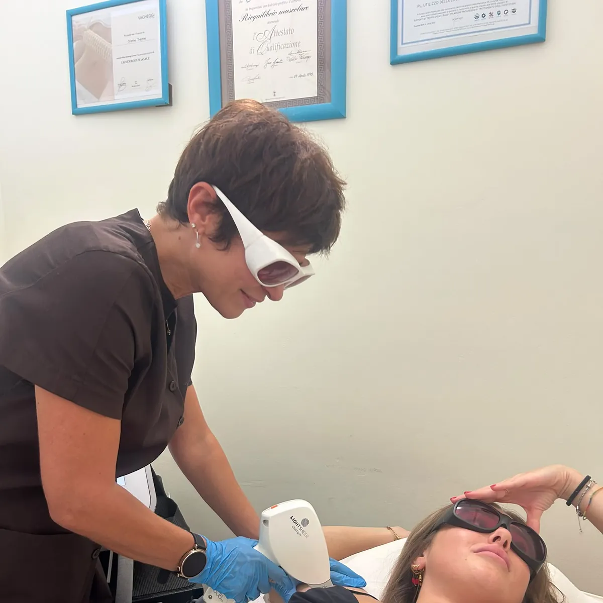 Alina durante un trattamento laser, con gli attestati di formazione alle spalle